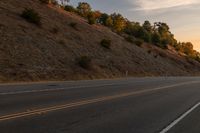 a person riding a motorcycle down the middle of an empty road at dusk with hills in background