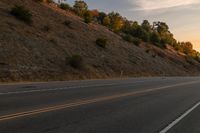 a person riding a motorcycle down the middle of an empty road at dusk with hills in background