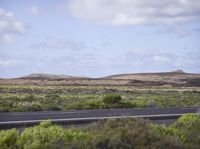 there is a man riding his motorcycle on the road in the desert near a field