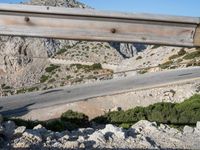 a man riding a motorcycle down the side of a mountain road in a canyon near the sea