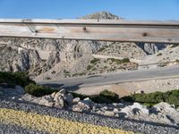 a man riding a motorcycle down the side of a mountain road in a canyon near the sea