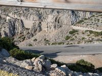 a man riding a motorcycle down the side of a mountain road in a canyon near the sea