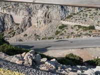 a man riding a motorcycle down the side of a mountain road in a canyon near the sea