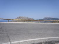 a person on a motorcycle riding on a road by a railing near the ocean and mountains