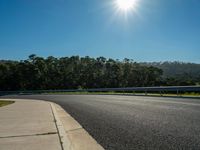 a man riding a motorcycle on an empty road near a wooded area with mountains in the distance