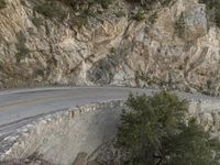 a person riding a motorcycle on a rock road next to trees and mountains with cliff cliffs