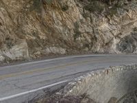 a person riding a motorcycle on a rock road next to trees and mountains with cliff cliffs