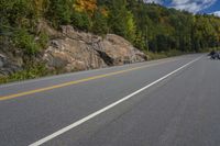 a motorcycle on the road with rocky cliffs in background, and trees lining the sides