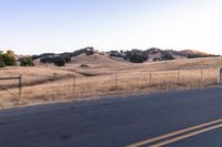 a man riding a motorcycle down the road by a fence in the middle of a field