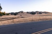 a man riding a motorcycle down the road by a fence in the middle of a field