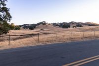 a man riding a motorcycle down the road by a fence in the middle of a field