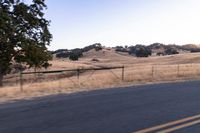 a man riding a motorcycle down the road by a fence in the middle of a field