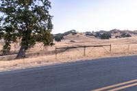 a man riding a motorcycle down the road by a fence in the middle of a field