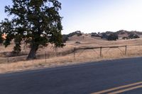 a man riding a motorcycle down the road by a fence in the middle of a field