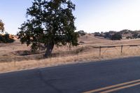 a man riding a motorcycle down the road by a fence in the middle of a field