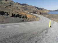 a person on a motor cycle down a mountain road near some water and cliffs behind them