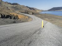 a person on a motor cycle down a mountain road near some water and cliffs behind them