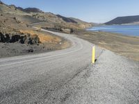 a person on a motor cycle down a mountain road near some water and cliffs behind them