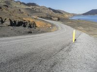 a person on a motor cycle down a mountain road near some water and cliffs behind them