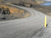 a person on a motor cycle down a mountain road near some water and cliffs behind them