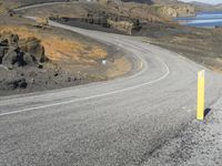 a person on a motor cycle down a mountain road near some water and cliffs behind them