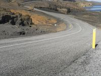 a person on a motor cycle down a mountain road near some water and cliffs behind them