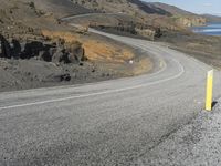 a person on a motor cycle down a mountain road near some water and cliffs behind them