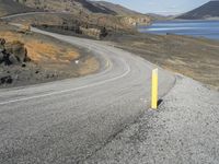 a person on a motor cycle down a mountain road near some water and cliffs behind them