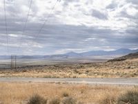 a person riding a motorcycle on the side of a road with a sky and mountains in the background