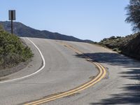 a woman rides a motorcycle down a winding road on a sunny day, in the middle of an arid area