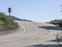 a woman rides a motorcycle down a winding road on a sunny day, in the middle of an arid area