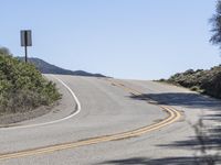 a woman rides a motorcycle down a winding road on a sunny day, in the middle of an arid area