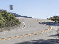 a woman rides a motorcycle down a winding road on a sunny day, in the middle of an arid area