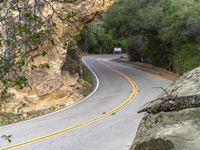 a motorcycle rides down the winding road between two rocks and greenery hills below a mountain