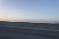 a person on a motorcycle rides along the side of a bridge at dusk, with the sun in the background