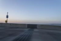 a person on a motorcycle rides along the side of a bridge at dusk, with the sun in the background