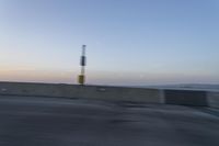 a person on a motorcycle rides along the side of a bridge at dusk, with the sun in the background