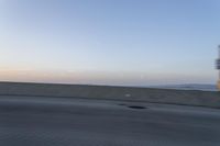 a person on a motorcycle rides along the side of a bridge at dusk, with the sun in the background