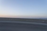 a person on a motorcycle rides along the side of a bridge at dusk, with the sun in the background