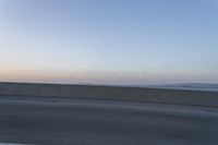 a person on a motorcycle rides along the side of a bridge at dusk, with the sun in the background