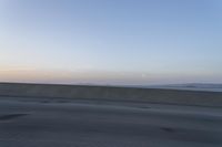 a person on a motorcycle rides along the side of a bridge at dusk, with the sun in the background