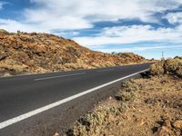 the motorcycle rider has his bicycle on the empty road by the rocks and hills at the bottom