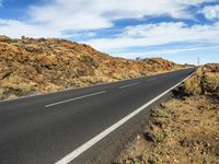 the motorcycle rider has his bicycle on the empty road by the rocks and hills at the bottom