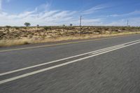 a motorcycle rider riding on an empty road in front of a mountain range with some grass and bushes