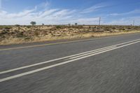 a motorcycle rider riding on an empty road in front of a mountain range with some grass and bushes