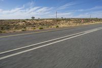 a motorcycle rider riding on an empty road in front of a mountain range with some grass and bushes