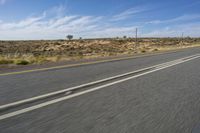 a motorcycle rider riding on an empty road in front of a mountain range with some grass and bushes