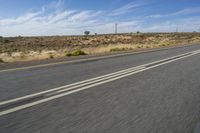 a motorcycle rider riding on an empty road in front of a mountain range with some grass and bushes