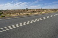 a motorcycle rider riding on an empty road in front of a mountain range with some grass and bushes