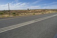 a motorcycle rider riding on an empty road in front of a mountain range with some grass and bushes